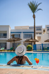 Fototapeta na wymiar Pretty woman in a hat enjoying cocktail in a swimming pool