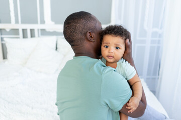 African-American dad hugs baby son holding him at home, happy family, Father's Day