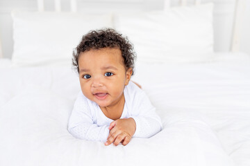 cute African-American little baby lying on a white bed in the bedroom of the house