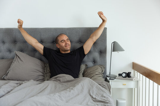 Content man stretching on bed after awakening