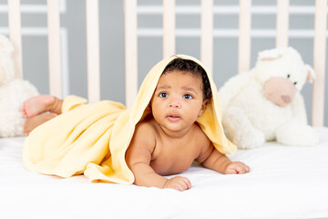 cute African-American little baby lying in bed after a bath in a yellow towel