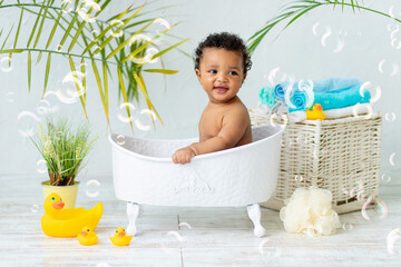 Happy laughter baby African taking a bath while playing with foam bubbles. A small child in the...