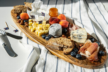 Fototapeta na wymiar Cheese platter with different cow and goat cheeses, meat, nuts, Summer fruits and berries, jam and rye bread on wooden board.on white table.