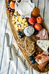 Cheese platter with different cow and goat cheeses, meat, nuts, Summer fruits and berries, jam and rye bread on wooden board.on white table.