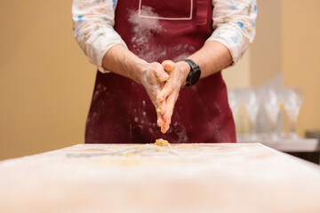 Man's hands are stained with dough after cooking. The man in the apron shakes the dough off his hands. Close-up.