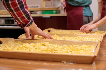 The pasta, cut into long strips, lies on a wooden tray. Use your hands to stir the raw pasta for cooking. Close-up.