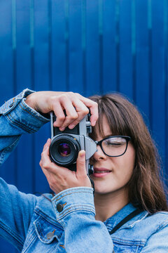 Woman taking photo on retro camera against blue wall