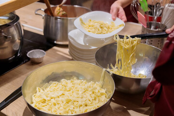 The chef prepares pasta in large metal pans. Male hands spread pasta on a plate. Close-up.