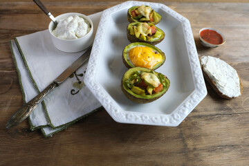 baked avocado stuffed with egg, vegetables, lie on a white dish, bread smeared with curd mass, linen napkin with embroidery, concept of post-holiday detox, diet, healthy food