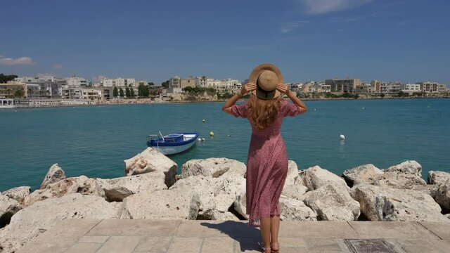 Young woman wearing dress and hat walking towards Otranto coast, Salento, Italy