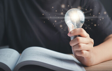Idea, Self learning, Education knowledge, Studying concept. Human hand hold light bulb or lamp and read textbook thinking ideas or new ideas futuristic.