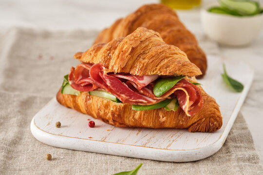 Fresh croissant or sandwich with cucumber, ham, Jamon, prosciutto, on wooden background. Morning breakfast concept. Healthy and fast food.