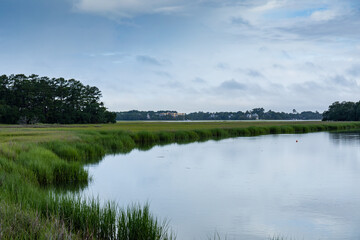 Sweeping waterway through a grassy salt marsh, treeline and early morning clouds and reflection, Mount Pleasant South Carolina, horizontal aspect