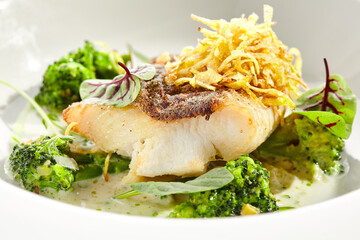 Panfried Fish with broccoli and cream sauce. Healthy roasted cod with green leaves. Fried Fish on white restaurant plate isolated on white background.