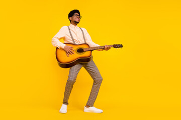 Photo of cheerful guy play guitar enjoy concert wear eyewear suspenders shirt isolated yellow color background