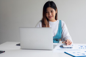 Portrait of Asian young woman working from home , laptop computer and analyzing real estate investment data Financial and tax systems concept.