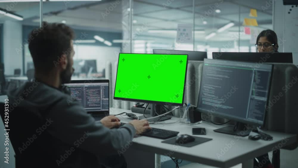 Fototapete Multi-Ethnic Office: IT Programmer Working on Computer with Green Screen Chroma Key Display. Male Software Engineer Developing App, Program, Video Game. Terminal with Code Language. Over Shoulder Shot