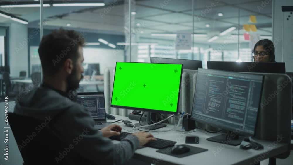 Poster Multi-Ethnic Office: IT Programmer Working on Computer with Green Screen Chroma Key Display. Male Software Engineer Developing App, Program, Video Game. Terminal with Code Language. Over Shoulder Shot