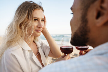 Portrait of a young couple sitting on the beach and drinking wine