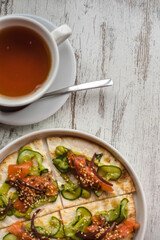 bread tortilla with salmon cucumber sauce and sesame along with tea on a white wooden background. healthy food background texture pita with red fish vegetables and sesame sprinkles. 
