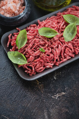 Close-up of raw fresh ground beef meat with green basil, vertical shot on a brown stone surface