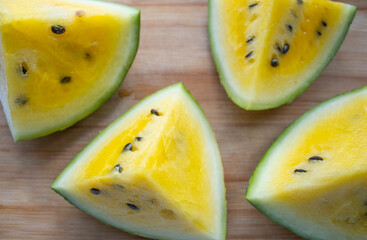 pieces of watermelon with yellow pulp and seeds, lie on a wooden board, on a light surface. Diet,...