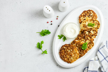 Crispy zucchini chicken fritters on white dish with sour cream sauce. Top view, space for text.