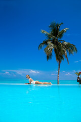 Elegant sexy woman in the white bikini on the sun-tanned slim and shapely body is posing near the swimming pool on Maldives island. Perfect body bikini model in luxury resort on Maldives.Luxury travel