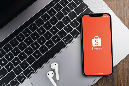 Shopee app on the smartphone screen on wooden background with a computer beside it. Top view. Rio de Janeiro, RJ, Brazil. August 2021.