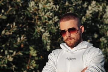 Portrait of young bearded man with tattoos in white jacket in countryside