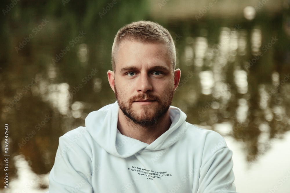 Wall mural portrait of young bearded man with tattoos in white jacket in countryside