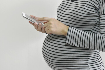 Pregnant woman using smartphone on gray background.