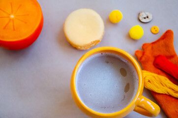 Obraz na płótnie Canvas Selective focus on orange cup of cappuccino next to macaron, persimmon and other decor on beige paper background. Autumn mood composition. Hugge concept with copy space. Top view, flat lay.
