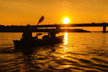 Silhouettes of people in boat at sunset. Man and woman ride boat on river. Small family trip