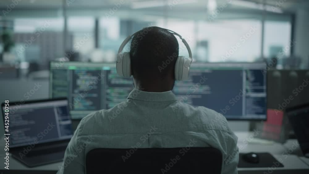 Wall mural office: professional black it programmer uses headphones while working on desktop computer. male web