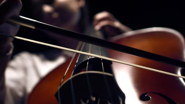 Bow and strings of cello closeup, down view. Concept of playing an instrument and enjoying music. Macro on black background