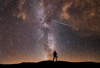 Fototapeta premium Beautiful starry night, photographer silhouette with camera looks at the Milky Way galaxy. Night landscape, astronomical background.
