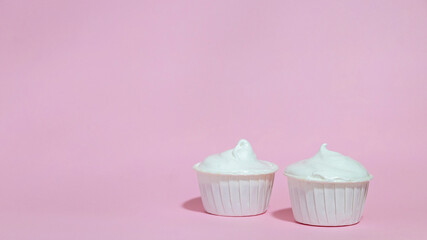 Two cupcakes in white shapes and white cream on a pink background. A place for the advertising text. Selective focus.
