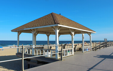 Well-kept pavilion with benches on boardwalk in front of beach (sand and shore) 