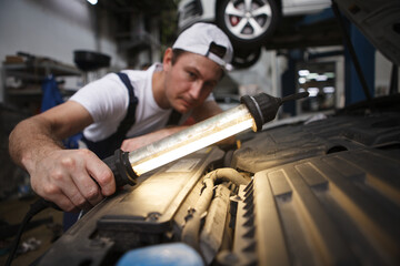 Fototapeta na wymiar Selective focus on a lamp in the hand of car repairman at the garage