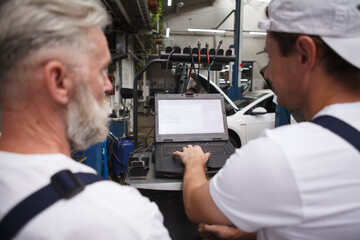 Close up rear view shot of two professional repairment using computer at car workshop