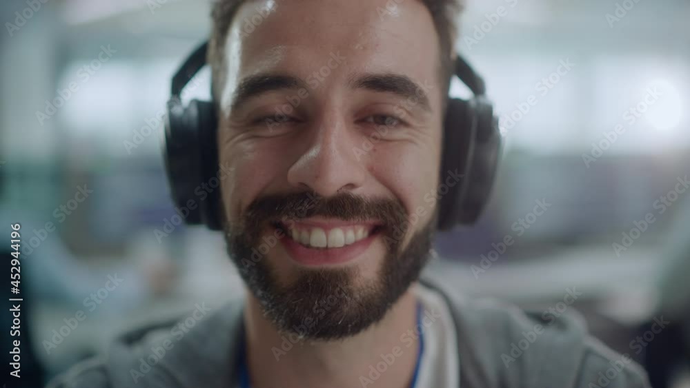 Poster Office: Portrait of Happy IT Programmer Wearing Headphones Working on Computer, Looking at Camera and Smiling. Male Software Engineer Developing App, Video Game. Listening to Podcast, Music. Close-up