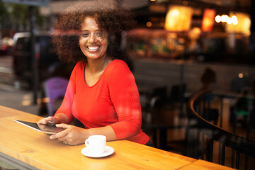 Young woman at cafe drinking coffee. Beautiful African girl using tablet while drinking coffee