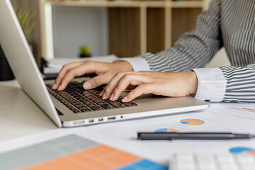 A businesswoman typing on a laptop keyboard, she is preparing a financial summary to bring to a meeting with business partners. Concept of company financial management. Checking financial information.