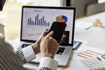 A businesswoman is holding a smartphone and using it, she is using a smartphone to send text messages to a company partner about financial statements. Concept of using technology in communication.