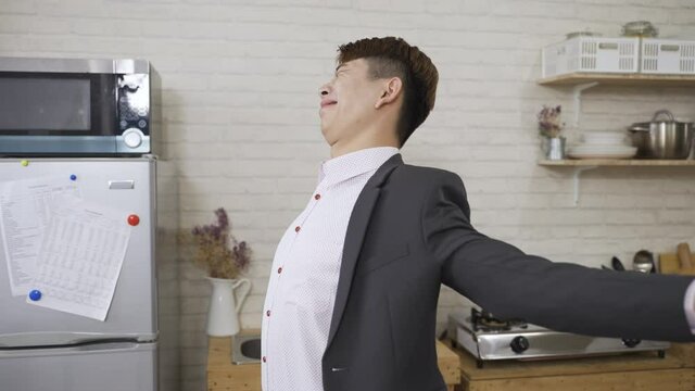 exhausted asian businessman walking up into the kitchen is stretching arms, exercising stiff neck and relaxing sore body in the morning before work at home.