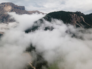 View from the drone to the forest and mountains  in the Dolomites of South Tyrol. Flying over the clouds in the Italian Alps