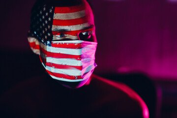 Adult man in medical face mask with USA flag on his face in the dark