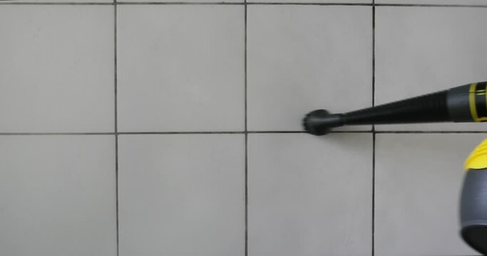 Stem pressure cleaner nozzle with brush attachment cleaning dirty faience floor tiles. Close up shot, real time, no people