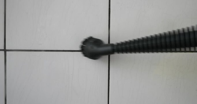 Stem pressure cleaner nozzle with brush attachment cleaning dirty faience floor tiles. Close up shot, real time, no people